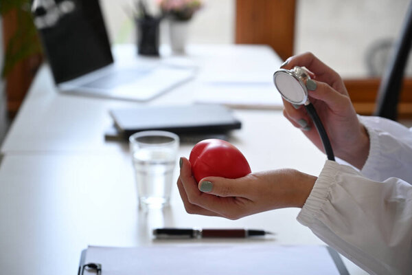 Крупным планом доктор держит красное сердце и стетоскоп. Концепция здравоохранения и кардиологии.