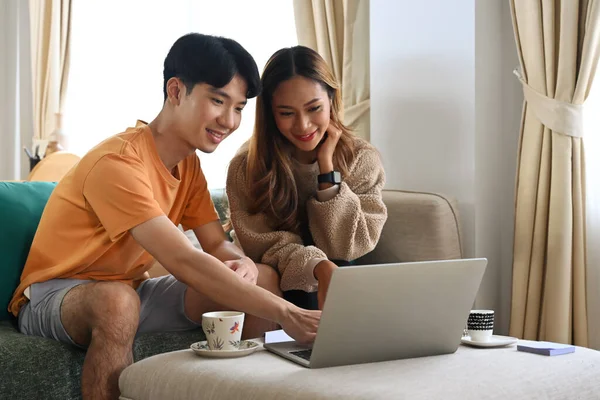 若いカップルがリビングルームに座って コンピュータのラップトップでオンラインショッピング — ストック写真