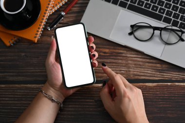 Yukarıda genç bir kadın ahşap masada akıllı telefon kullanıyor..