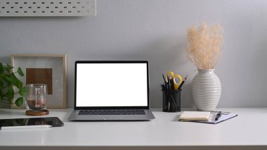 Boş ekran, defter, kahve fincanı ve beyaz masadaki bitki örtüsü ile ön görünüm dizüstü bilgisayarı.