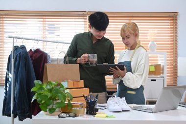 İki mutlu küçük iş ortağı dijital tablette ürün satın alma siparişini kontrol ediyor ve teslimat için paket hazırlıyor.