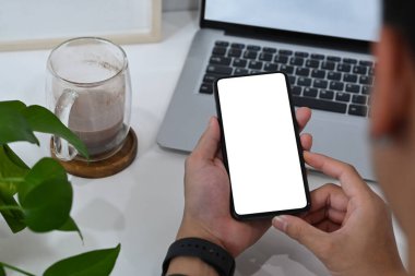 Yakın plan genç adam modern işyerinde oturuyor ve akıllı telefon kullanıyor..