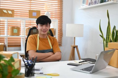 Küçük işletme girişimcisi ofiste kollarını kavuşturup kameraya gülümsüyor..