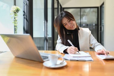 Gülümseyen Asyalı girişimci kadın cep telefonuyla konuşuyor ve deftere not alıyor.. 