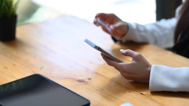 Kesilmiş, genç bir kadın kredi kartı tutuyor ve akıllı telefon kullanıyor..