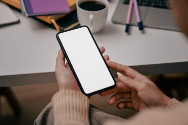 Omzunun üstünden bak genç bayan ofis masasında oturuyor ve akıllı telefon kullanıyor..