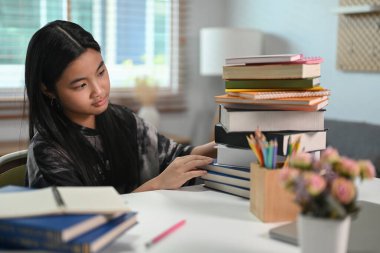 Asyalı ilkokul öğrencisi bir yığın kitapla oturuyor. Eğitim kavramı.