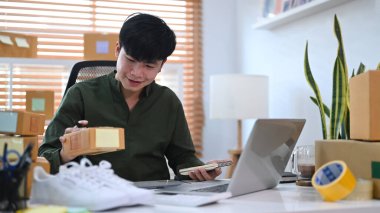 Başlangıçta küçük işletme sahibi dizüstü bilgisayarda ürün satın alma siparişini kontrol ediyor ve teslimat için ürün paketliyor.