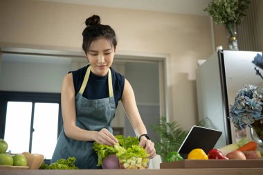 Önlüklü gülümseyen kadın mutfakta sağlıklı organik salata yapıyor. Sağlıklı yaşam tarzı kavramı.