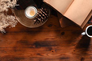 Kaliteli kitap, kahve fincanı, mum ve çam kozalağı ahşap masada..