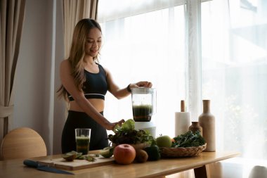 Gülümseyen Asyalı genç kadın mutfakta sağlıklı meyve suyu yapıyor..