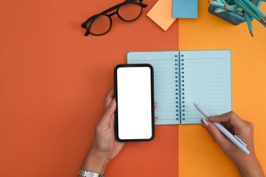 El ele tutuşan akıllı telefon ve not defterine notlar alan bir kadın..