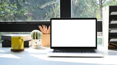 Boş ekranlı bilgisayar, kaktüs ve kahve fincanı parlak oturma odasında beyaz masada..