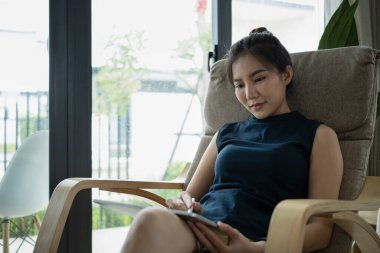 İnternette dijital tabletle sörf yapan güzel bir kadın rahat koltukta dinleniyor..