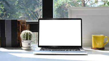 Mokup laptop bilgisayar, resim çerçevesi, kitaplar ve kaktüs beyaz masa üzerinde parlak ev ofisinde.