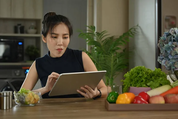 Woman using digital tablet in kitchen for recipe. Healthy lifestyle concept.