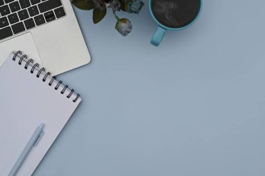 Not defteri, bilgisayar dizüstü bilgisayar, kahve fincanı ve mavi arka planda saksı. Düz yatış, Üst Görünüm.