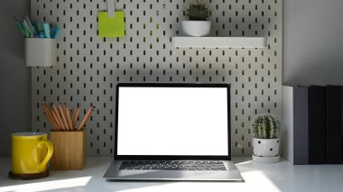 Önde dizüstü bilgisayar, kahve fincanı ve malzemeler parlak oturma odasındaki beyaz masada..