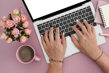 Pembe arka planda dizüstü bilgisayar kullanan genç bir kadın.