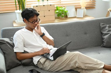 Asyalı adam kanepede dinleniyor ve bilgisayar tableti kullanıyor..