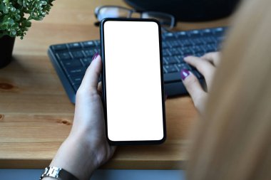 Görüntüyü kapat. Akıllı telefon tutan ve kablosuz klavyede yazan genç kadın..