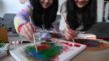 Kırpılmış iki neşeli Asyalı kız, birlikte vakit geçirirken oturma odasında resim çiziyor..