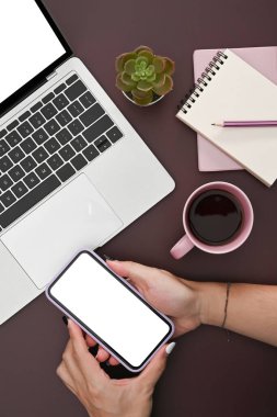 İş yerinde oturan ve grafik görüntüleme montajı için boş ekran ile akıllı telefon tutan kadının üstünde.