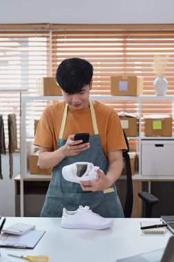 Merkez büroda çalışan genç bir adam internette satabilmek için akıllı telefonlu ayakkabılara fotoğraf çekiyor..