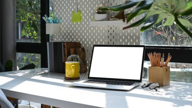 Dizüstü bilgisayarı, bitki örtüsünü ve kırtasiyeyi beyaz masaya yapıştır.