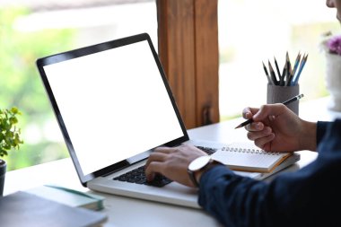 Dizüstü bilgisayarla çalışan ve deftere notlar alan kırpılmış bir iş adamı..