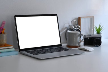 Dizüstü bilgisayarı, kamerası ve kahve fincanı olan çağdaş çalışma alanı beyaz masada..