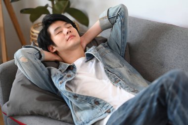 Memnuniyet duyan Asyalı adam ellerini başının arkasına koyup evdeki rahat koltukta dinleniyor..