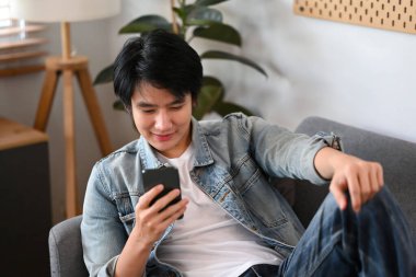 Kanepede oturup sosyal medyayı kontrol etmek için akıllı telefon kullanan mutlu bir adam..