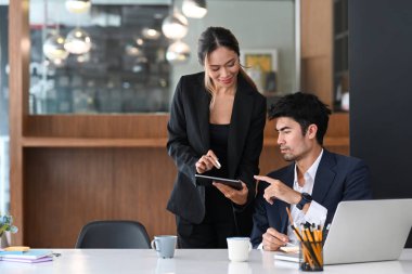 İki başarılı iş ortağı dijital tablet kullanıyor ve modern ofiste iş konularını tartışıyorlar..