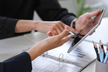 Profesyonel iş adamlarından oluşan bir ekip dijital tablet üzerindeki finansal verileri tartışıyor ve analiz ediyor.