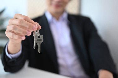 Emlakçı evin anahtarlarını tutuyor. Gayrimenkul yatırımı ve sigorta konsepti. Anahtarlar ile seçici odaklanma.