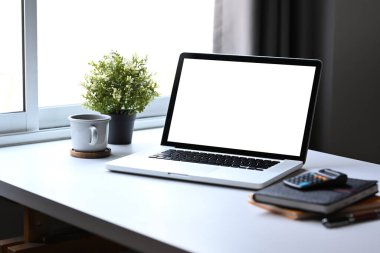 Bilgisayar dizüstü bilgisayar, hesap makinesi, kahve fincanı, beyaz masada saksı bitkisi. Merkez ofis iş yeri kavramı.