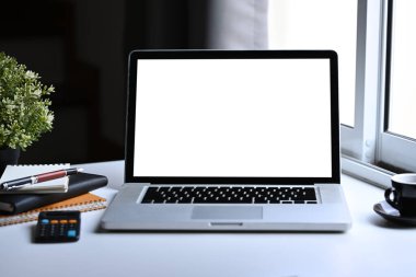 Ön görünüm model dizüstü bilgisayar, kahve fincanı, defter ve hesap makinesi beyaz ofis masasında..