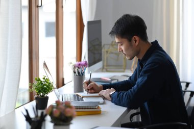 Parlak ofiste dizüstü bilgisayarla çalışan genç bir çalışan..