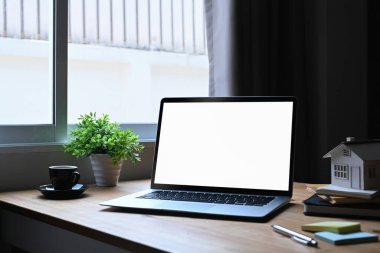 Laptop bilgisayar, ev modeli ve ahşap masada kahve fincanı. İpotek ve gayrimenkul yatırım kavramı.