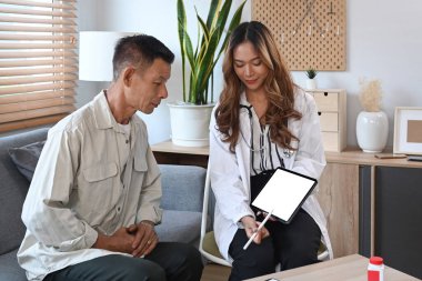 Dijital tablet tutan kadın doktor ve yaşlı erkek hastaya sağlık hizmetleri konusunda tavsiyelerde bulunuyor..