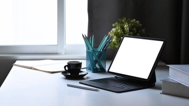 Kablosuz klavyeli dijital tablet, saksı çiçeği, kahve fincanı ve beyaz masadaki kırtasiye malzemesi..