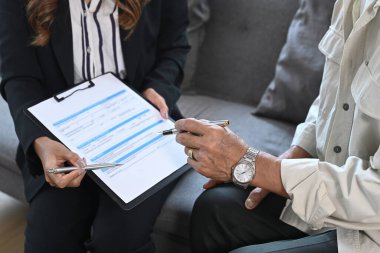 Sigorta bürosunda oturan ve sağlık sigortası anlaşmasını imzalayan yaşlı bir adamın kırpılmış görüntüleri..