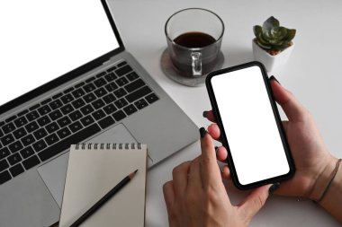 Ofis masasında bilgisayar laptopuyla oturan ve cep telefonu kullanan kadını kapat..