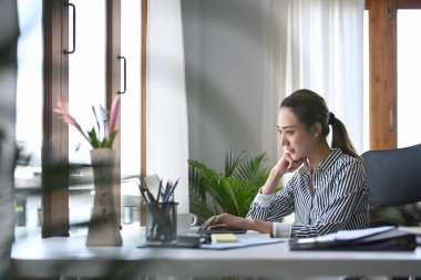 Parlak modern ofiste oturan ve dizüstü bilgisayar kullanan muhteşem genç bir kadın..