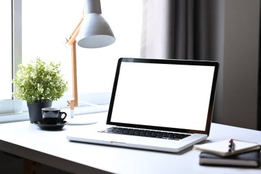 Mokup laptop bilgisayar, saksı bitkisi, kahve fincanı ve lamba parlak ev ofisinin beyaz masasında..