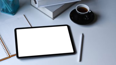 Dijital tablet, stilus kalem, kahve fincanı ve beyaz ofis masasındaki defter..