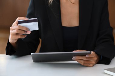 Kredi kartı tutan ve dijital tablet kullanan bir iş kadını. Çevrimiçi alışveriş, e-ticaret, internet bankacılığı kavramı.