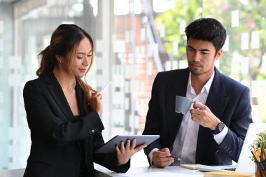 Fikirlerini paylaşan iki iş adamı strateji düşünüyor, modern işyerinde online sunumu tartışıyor.