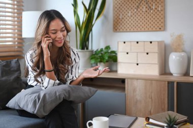 Çekici milenyum kadını evdeki koltukta dinleniyor ve cep telefonuyla konuşuyor..